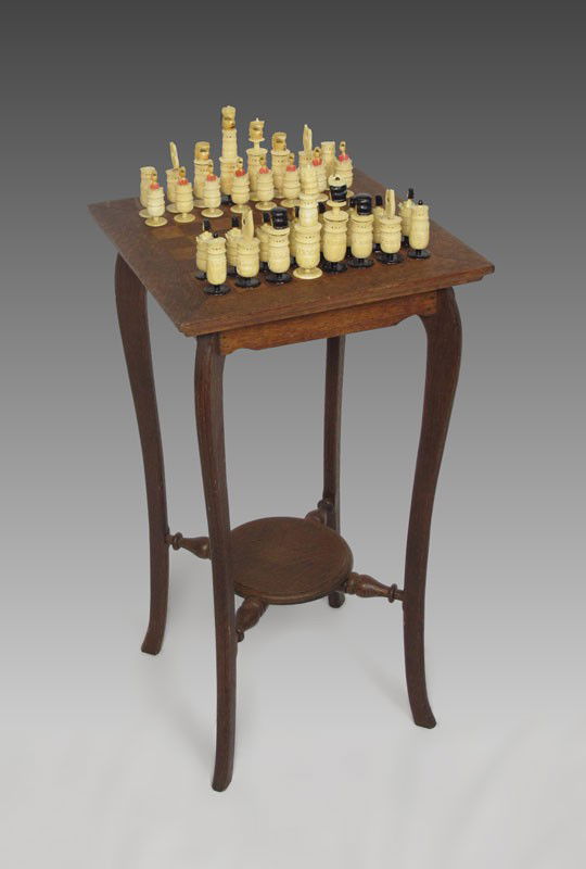 CARVED IVORY CHESS SET WITH TABLE: CARVED IVORY CHESS SET WITH TABLE: Inlaid chess board top trimmed in quarter sawn oak. Long shaped legs with round lower shelf leg support. Comes with complete ivory chess set. 30" h. x 16" x 16".