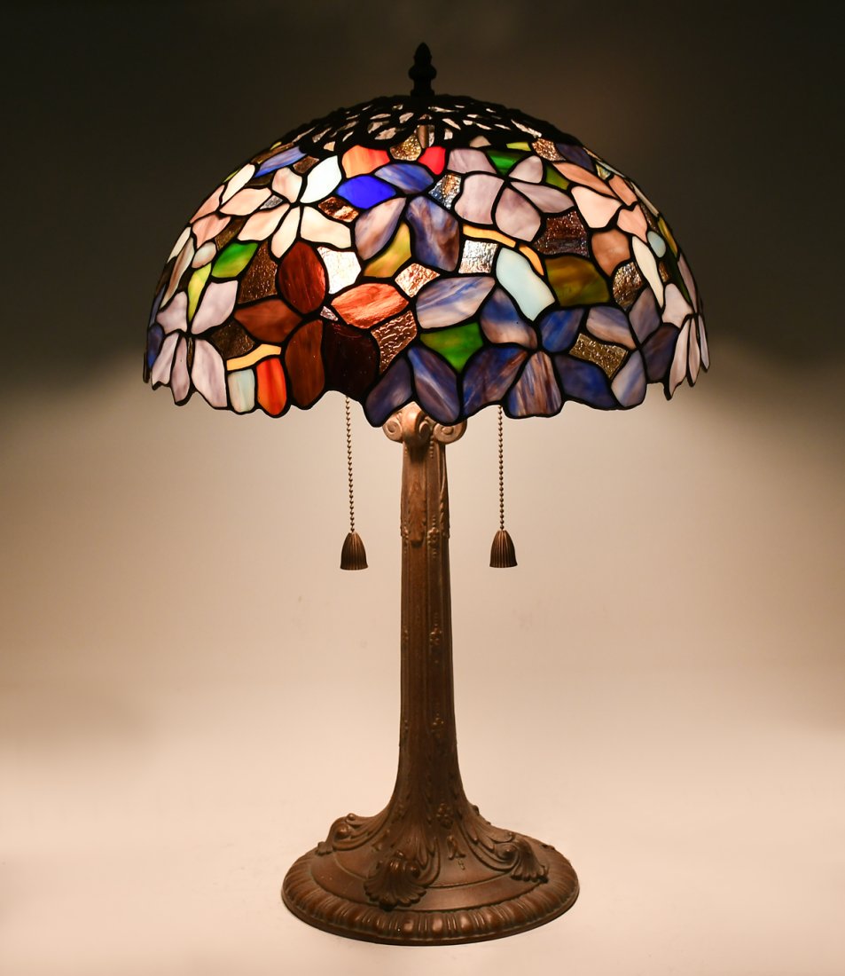 STAINED GLASS FLORAL LAMP: STAINED GLASS FLORAL LAMP: Colorful leaded glass shade, having a stylized floral motif. Shade resting upon a patinated metal, two light foliate motif base with Tassel form pulls. Approx. 24.5" h x 16"