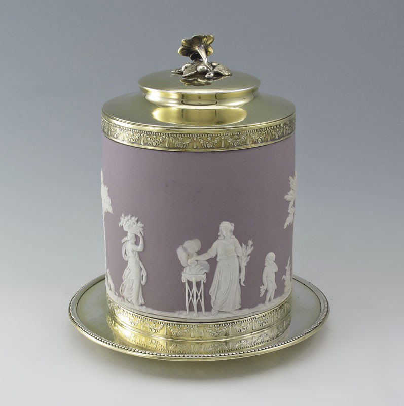 WEDGWOOD COVERED BISCUIT JAR: WEDGWOOD COVERED BISCUIT JAR: Purple Jasperware body with gold toned rim, lid with floral and under plate. Impressed Wedgwood. 8 1/4" h. x 7 1/2" dia. overall.