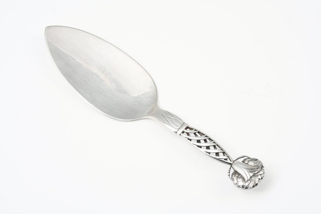 GEORG JENSEN "ORNAMENTAL 83" STERLING CAKE SERVER: GEORG JENSEN "ORNAMENTAL 83" STERLING CAKE SERVER: Approx. 2.70 Troy ounces. Comprising; 1- Danish Georg Jensen Cake Server, having a pierced handle terminating in a stylized flower. Approx. 8.75" l x
