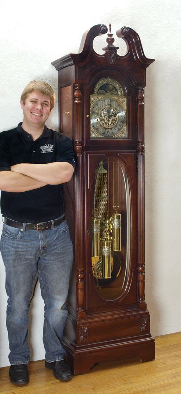 HOWARD MILLER STEWART MODEL GRANDFATHER CLOCK: HOWARD MILLER STEWART MODEL GRANDFATHER CLOCK: The ''Stewart'' model by Howard Miller with mahogany case. Broken arch pediment with spire finial, fluted half column decoration, illuminated interior. M
