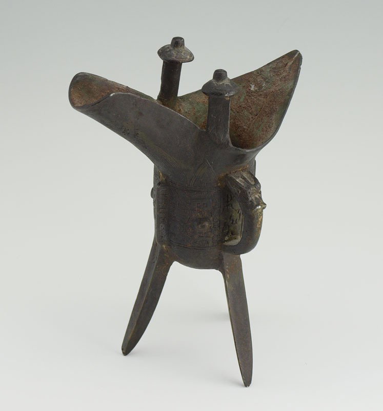 CHINESE SHANG DYNASTY STYLE BRONZE LIBATION CUP: CHINESE SHANG DYNASTY STYLE BRONZE RITUAL LIBATION CUP: Of jue elliptical form, one side of the top mouth rim molded in an outstretched spade form, the other as an elongated open channel spout, with 2