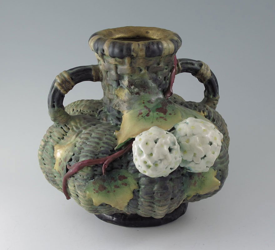 AMPHORA POTTERY BASKET WEAVE VASE: AMPHORA POTTERY BASKET WEAVE VASE: Double handled basket weave body vase with applied leaves and geraniums. Amphora pottery impressed marks. 7 3/4" h. x 8" x 9 1/2".