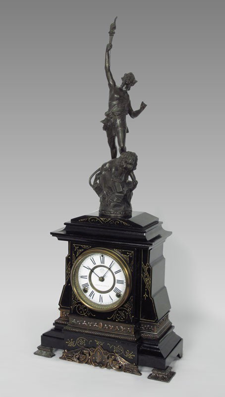 BLACK ANSONIA FIGURAL CLOCK: BLACK ANSONIA FIGURAL CLOCK: Cast metal figure of man holding torch above a lion. Cast iron base with faux slate appearance, porcelain dial marked Ansonia Clock Co. Ansonia key and pendulum, time and 