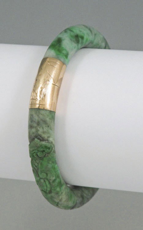 CARVED JADEITE JADE & 14K GOLD BANGLE BRACELET: CARVED JADEITE JADE & 14K GOLD BANGLE BRACELET: 14K yellow gold mounted bracelet, hinged closure with figure 8 clasp and safety chain, 81.5 mm dia., interior 2 1/2".
