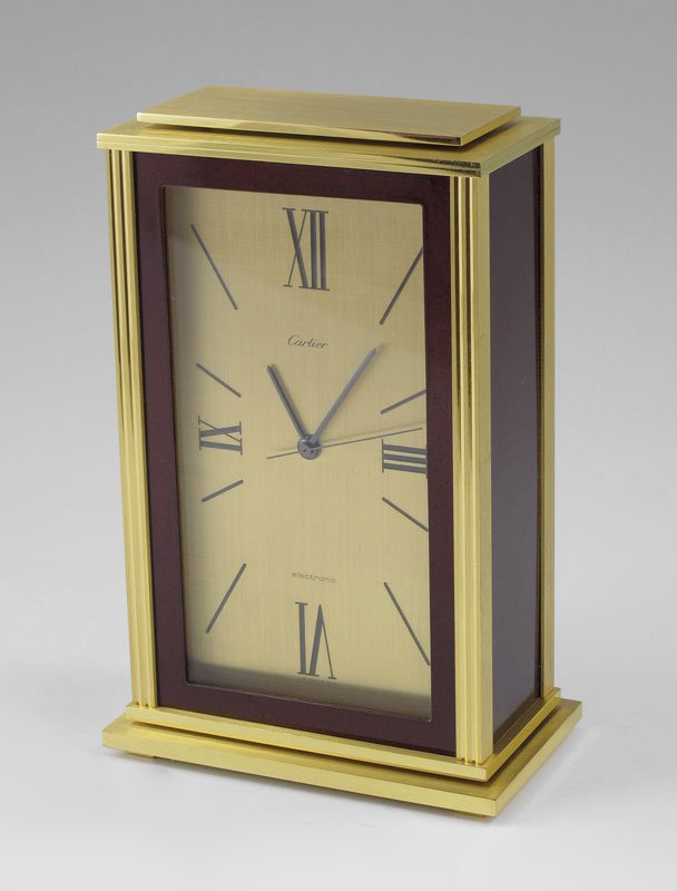 CARTIER DESK CLOCK IN PRESENTATION BOX: CARTIER DESK CLOCK IN PRESENTATION BOX: Brass case with inset faux red stone enamel sides and border. Brass face with Roman quarter hour numerals, battery powered quartz movement. Marked Cartier, elec