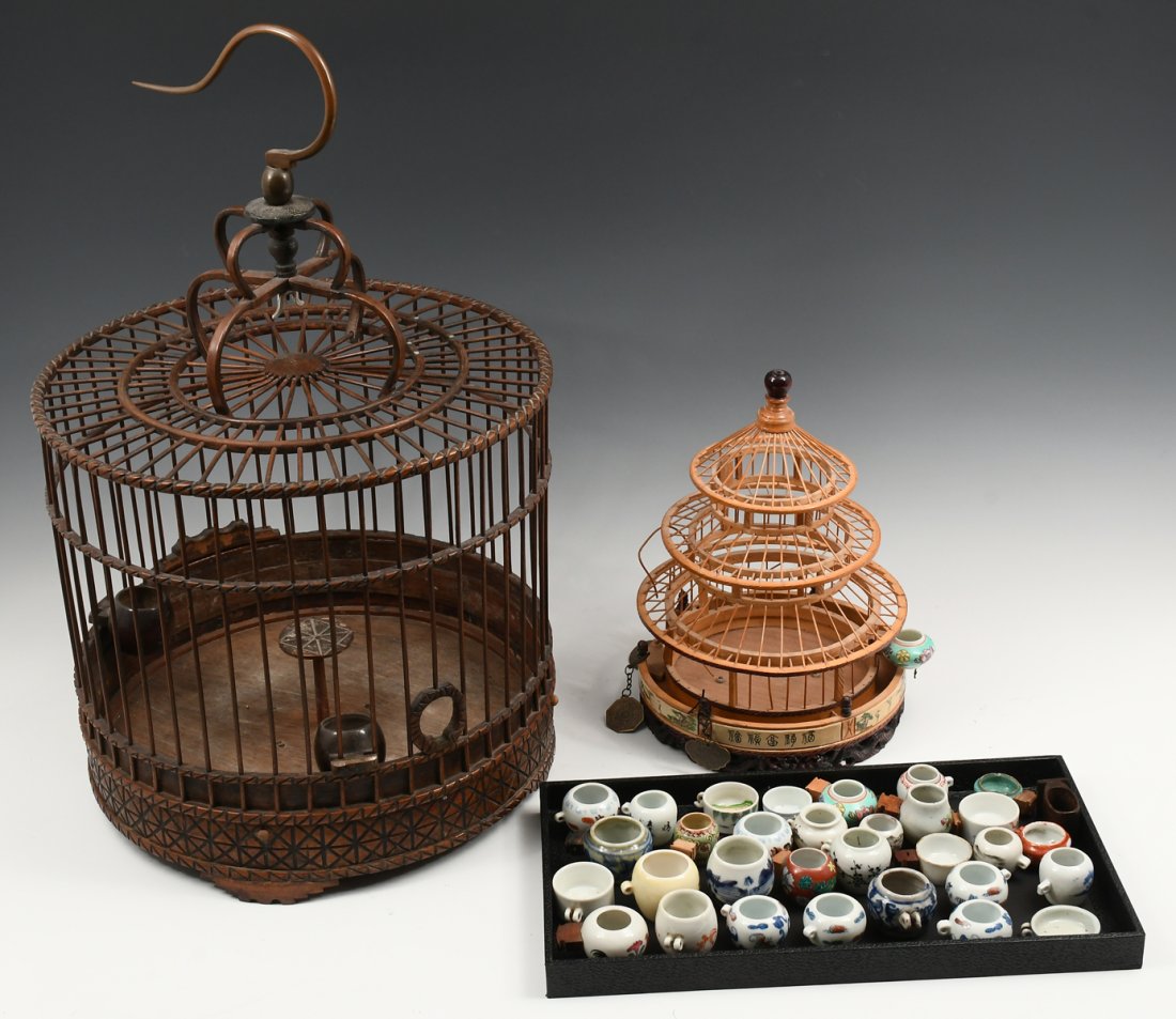 2 CHINESE BIRDCAGES WITH PORCELAIN SEED HOLDERS: 2 CHINESE BIRDCAGES WITH PORCELAIN SEED HOLDERS: The largest cage being cylindrical in form, approx. 12.5" h x 13.75" dia, topped by a hook 9.25" in length. The small, pagoda form cage being approx. 1