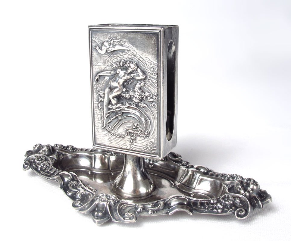 KERR MOUNTED ART NOUVEAU STERLING MATCHBOX HOLDER: KERR MOUNTED ART NOUVEAU STERLING MATCH BOX HOLDER: Holder with full figural nude woman in crashing surf, mounted to base with repousse floral, foliate, masquerons and cherub heads. Measures 3 3/8" h.