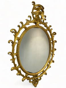 GILDED EAGLE MIRROR: GILDED EAGLE MIRROR: A carved giltwood & gesso mirror; the oval central looking glass framed by floral trim and ornate foliate scroll openwork frame with asymmetrical open-winged eagle crest and a