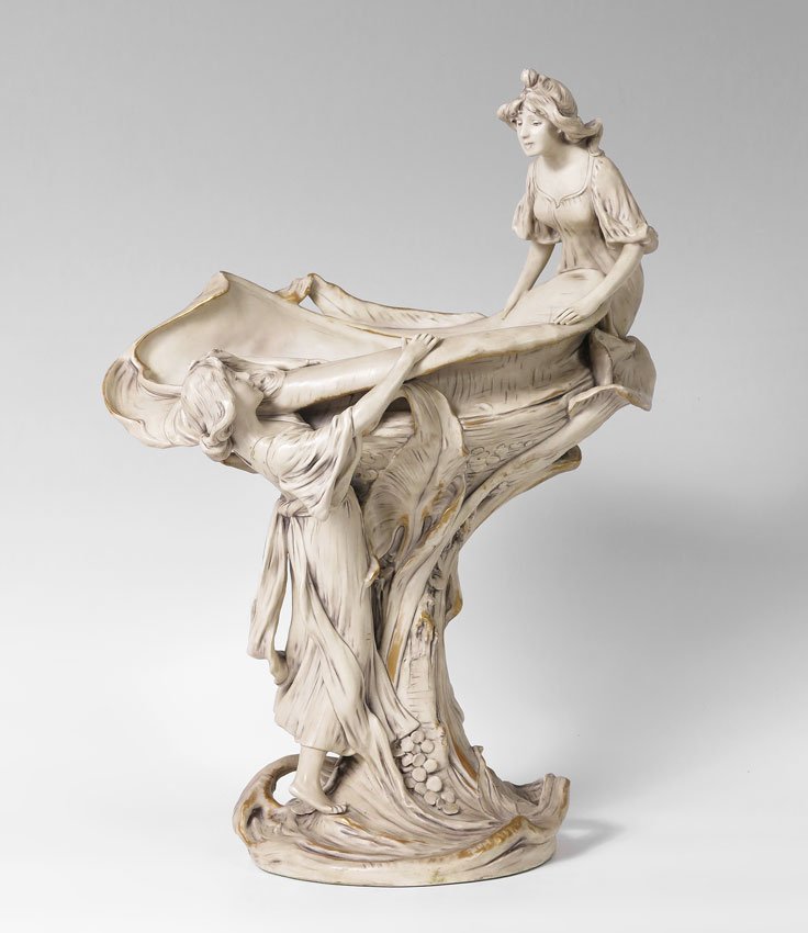 ROYAL DUX BOHEMIAN ART NOUVEAU FIGURAL CENTER BOWL: ROYAL DUX BOHEMIAN ART NOUVEAU FIGURAL CENTER BOWL: Ca. 1900-1947. Parcel gilt porcelain figural group of two maidens in a close interaction with nature. Drilled as for a lamp. Measures 21" tall x 15"