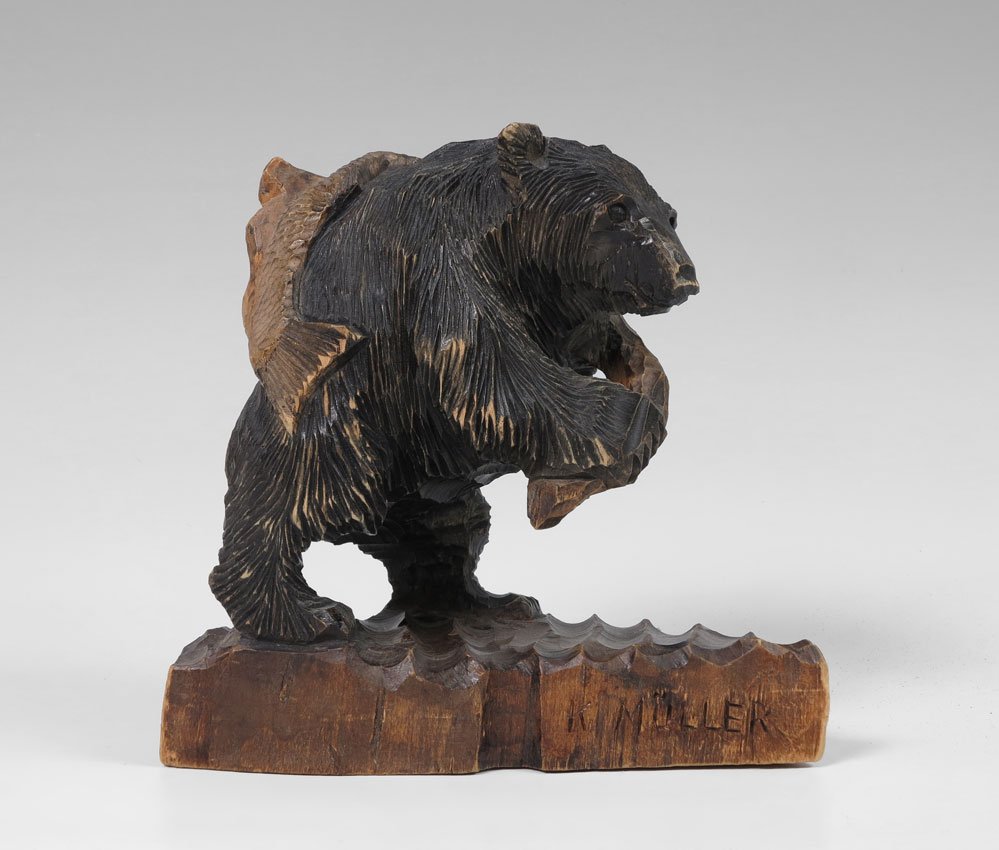 K. MULLER BLACK FOREST CARVED BEAR: K. MULLER BLACK FOREST CARVED BEAR: Whimsical carved bear holding a rope with fish on back. Signed K. Muller on base. 8 1/2'' h. x 8 3/4'' x 4 1/2''.