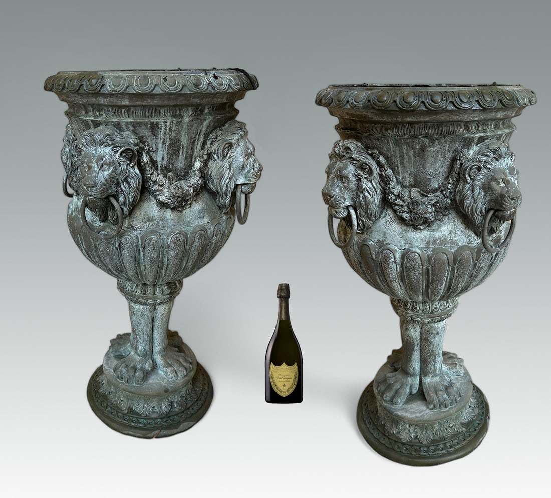 A MAJESTIC PAIR OF BRONZE LION HANDLED URNS: A MAJESTIC PAIR OF BRONZE LION HANDLED URNS: Palatial Bronze Urns with Draped Floral strands alternating with Lion's heads with Rings hanging from their jaws. Approx. 46" h x 26.5" w. From the mega-mi