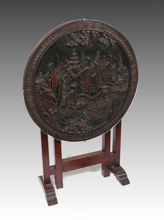 CARVED CHINESE TILT TOP TABLE: CARVED CHINESE TILT TOP TABLE: Glass top over carved coastal scene with ships, buildings and figures. 24 1/2" h. x 23 3/4" dia. when down.