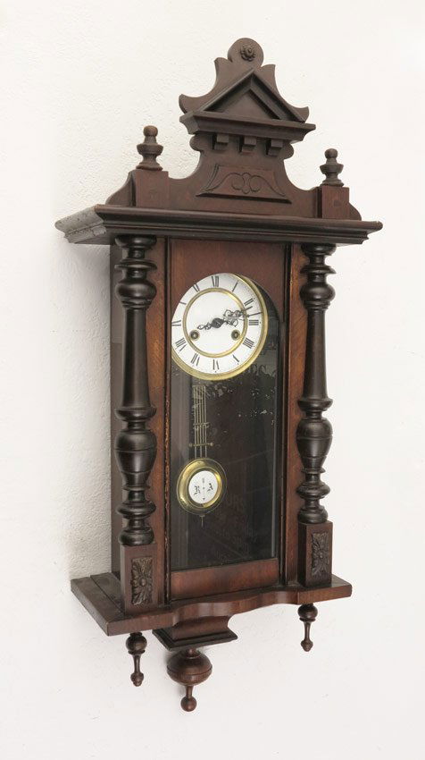 CARVED GERMAN REGULATOR WALL CLOCK: CARVED GERMAN REGULATOR WALL CLOCK: Architectural crest with 2 finials, dark wood case with applied decoration. Porcelain dial, time and strike movement. Key in office, pendulum in case. 36 1/2'' h. x