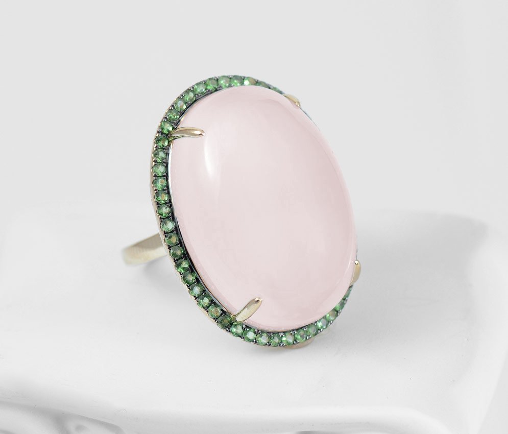 14K GOLD ROSE QUARTZ & TSAVORITE GARNET RING: ROSE QUARTZ & GREEN TSAVORITE GARNET RING: 14K gold ring centering an approx. 31.20 Ct oval shaped cabochon rose quartz framed in green tsavorite garnets totaling approx. .63 Ct. Size 6.5 Sold with cu