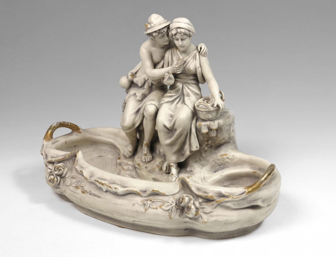 FIGURAL ROYAL DUX CENTER BOWL: FIGURAL ROYAL DUX CENTER BOWL: Figures of seated lovers with flower and basket. Gilt highlights. Royal Dux Bohemia ''E'' mark, dates from 1900-1918, impressed 1965 on base. 10 1/2'' h. x 14 1/2'' x 8 