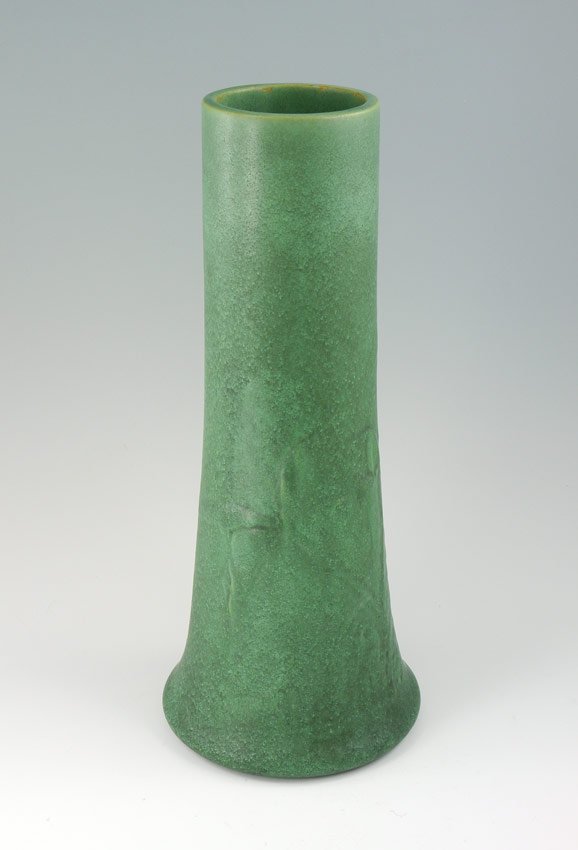 TECO POTTERY VASE RELIEF LILY DESIGN: TECO POTTERY VASE RELIEF LILY DESIGN: Flared base, cylindrical form with relief decoration of lilies or iris, green matte glaze. Impressed Teco mark center of base. 13'' h. x 5 1/2'' dia.