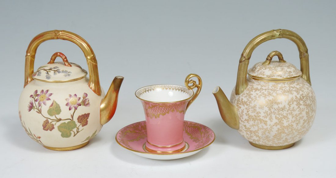 ROYAL WORCESTER 2 TEAPOTS, CUP AND SAUCER: ROYAL WORCESTER TEAPOTS, CUP AND SAUCER: Two teapots in the same form with bamboo type handles, 6 1/2 x 6 1/2" overall. Sold together with a tall parcel gilt cup and saucer, also Royal Worcester.