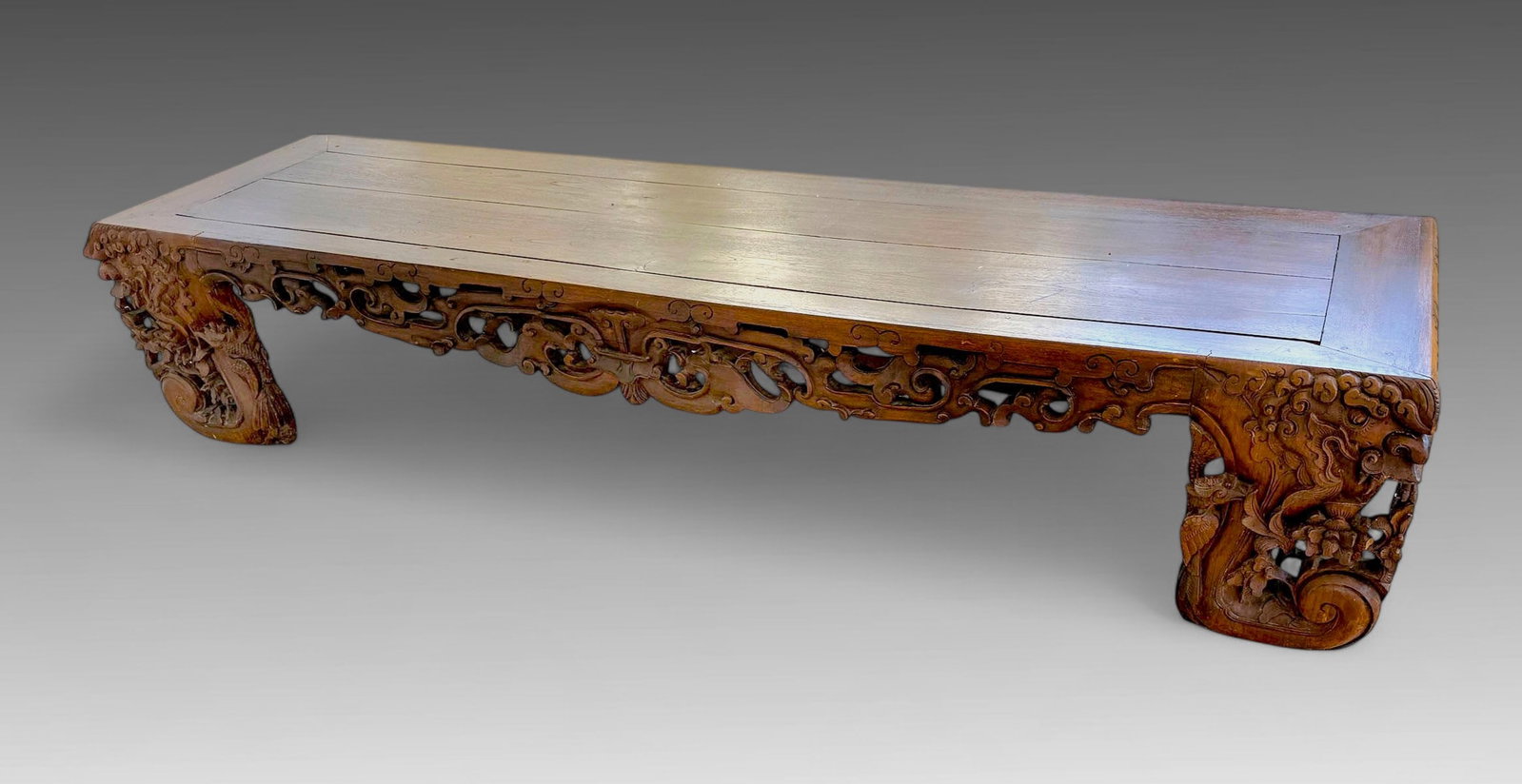 HIGH-RELIEF CARVED CHINESE QING DYNASTY LOW TABLE: HIGH-RELIEF CARVED CHINESE QING DYNASTY LOW TABLE: Wood & Tenor constructed Chinese Hardwood table, having a pierced Apron with a stylized Bat & Dragon Motif. Approx. 17.5" h x 89.5" l x 23.25" w.