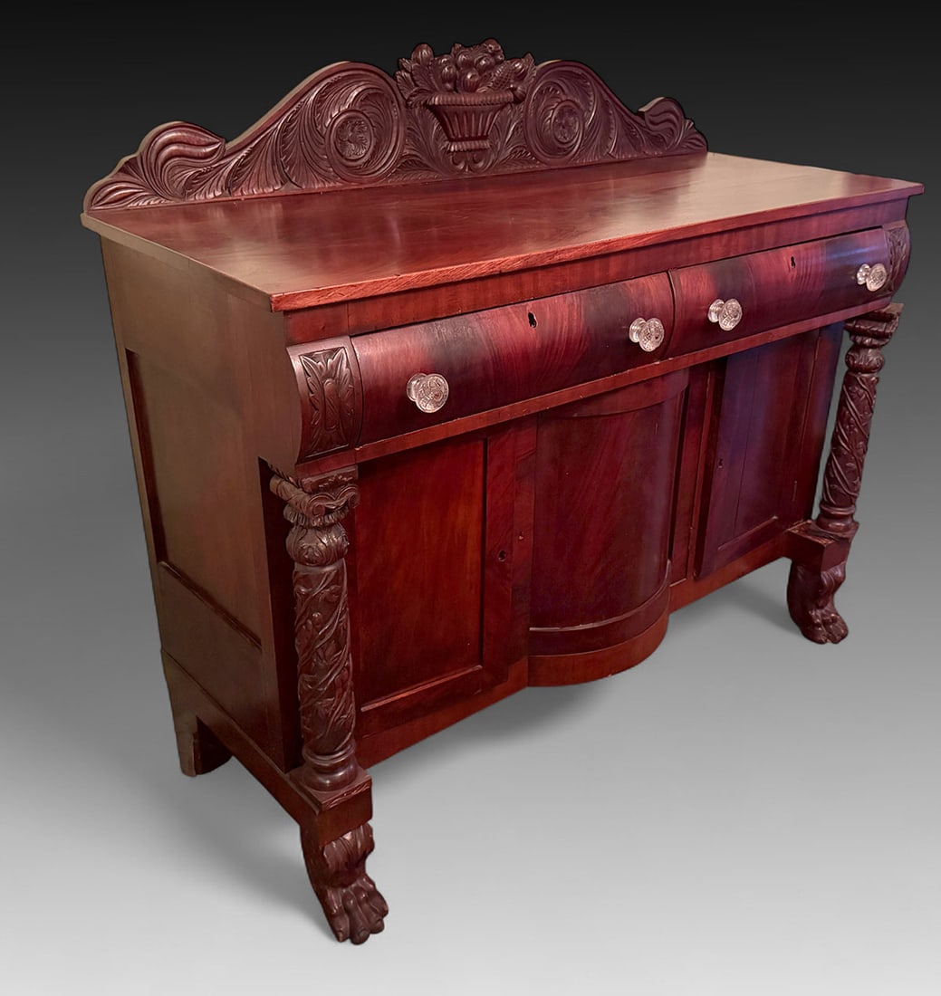 AMERICAN EMPIRE CARVED BUFFET: AMERICAN EMPIRE CARVED BUFFET: American Empire Buffet surmounted by a carved Bountiful Basket crest rail with scrolled foliate and floral medallions. 2- Drawers over 3- Doors, flanked by Spiraling Vin
