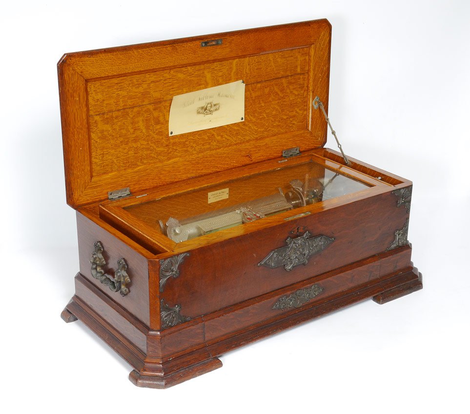 JACOT & SON SWISS CYLINDER MUSIC BOX: JACOT & SON SWISS CYLINDER MUSIC BOX: Tiger oak case with applied metal decoration including bust of Orpheus. Celluloid tag under lid reads Ideal Sublime Harmonie over Orpheus over illegible writing.