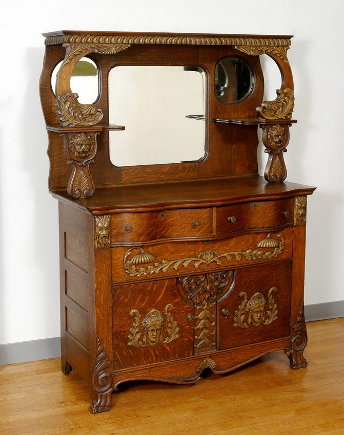 CARVED AMERICAN GOLDEN OAK SIDEBOARD: CARVED AMERICAN GOLDEN OAK SIDEBOARD: Carved decoration to include figural dolphin heads, lion and maiden masquerons. Top with 3 beveled mirror and 2 open shelves. Base with serpentine top and 2 half 