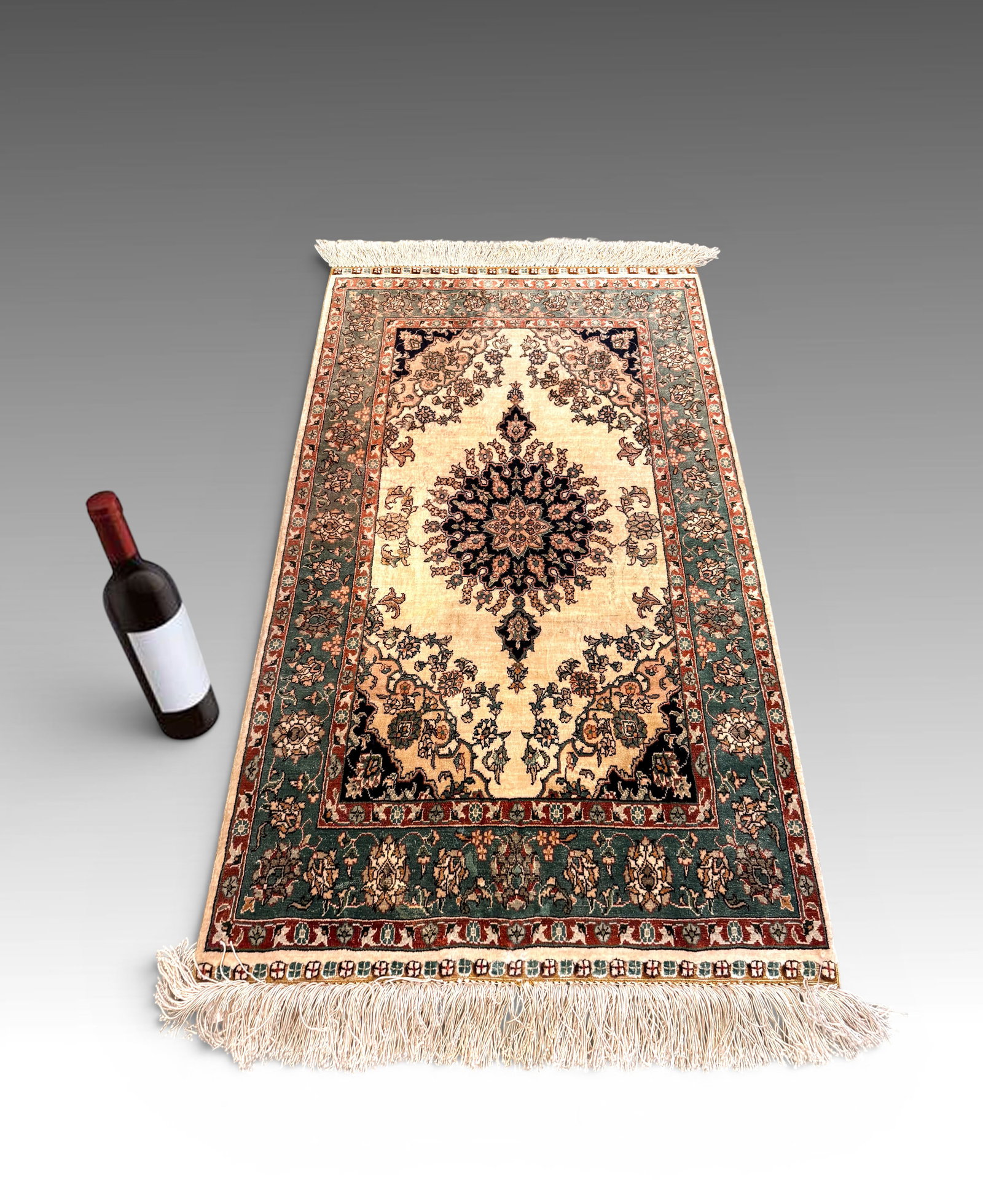 SILK ORIENTAL ESTATE RUG 36" X 24.25": SILK ORIENTAL ESTATE RUG: Small accent rug with black central medallion and pennants on a cream field. Teal main border, burgundy secondary border, white fringes. Measures 36" x 24.25".