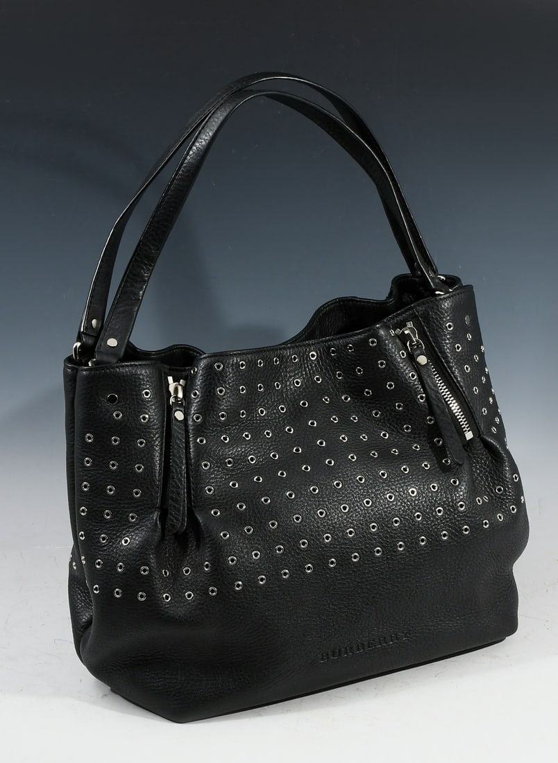 BURBERRY MAIDSTONE EYELET LEATHER BAG: BURBERRY MAIDSTONE EYELET LEATHER BAG: An edgy Burberry black leather large Maidstone eyelet Bag is crafted of black pebbled leather with silvertone grommets (eyelets) The sides have zipper detains to