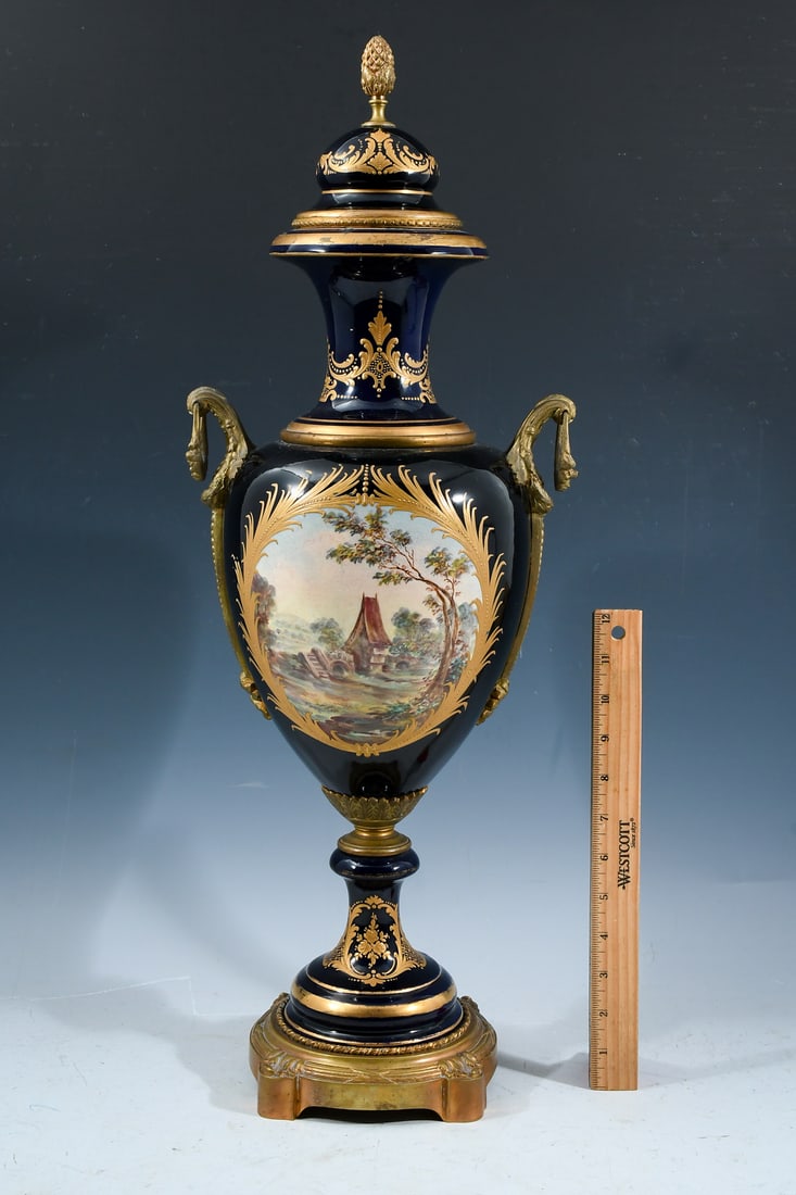 COBALT SEVRES STYLE METAL MOUNTED COVERED URN: COBALT SEVRES STYLE METAL MOUNTED COVERED URN: Cobalt blue ground with hand-painted scenes of women smoking and a countryside cottage. Heavy gold enameled foliate motif. Signed with the Interlaced L's