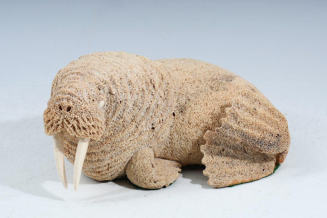 FOSSILIZED WHALE BONE INUIT CARVED WALRUS: FOSSILIZED WHALE BONE INUIT CARVED WALRUS: A carved whalebone sculpture of a Walrus, handcrafted by Ekemo Studios of Eagle River, Alaska. Approx. 4" h x 8" w x 6.5" d.