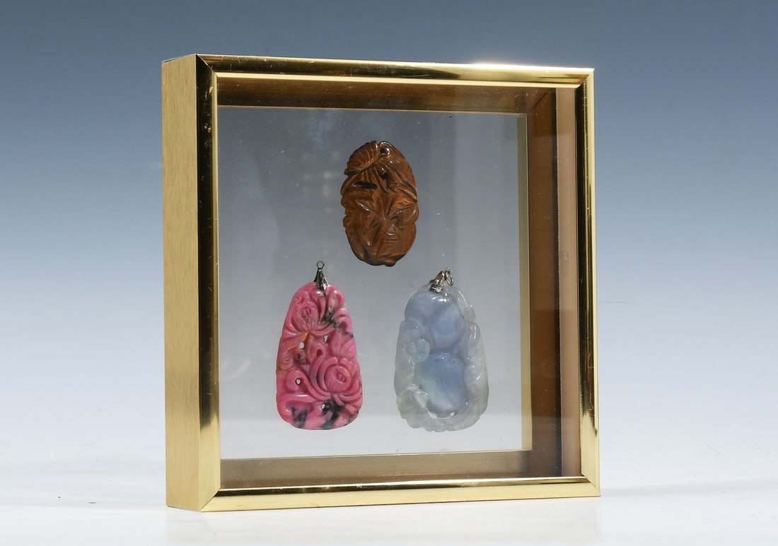3 PC. CARVED CHINESE MINERAL STONE PENDANTS: 3 PC. CARVED CHINESE MINERAL STONE PENDANTS: Framed carved Chinese Pendants. Comprising; 1- Tiger's Eye Floral motif pendant, 1- Rhodonite Floral motif Pendant, & 1- Amethyst Quartz Auspicious