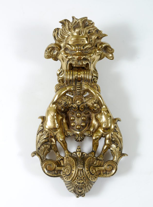 HEAVY CAST METAL FIGURAL DOOR KNOCKER: HEAVY CAST METAL FIGURAL DOOR KNOCKER: Figural head cleat with knocker comprising of 2 putti and foliate motif. Unmarked to maker. Measures 12 1/4" h. x 6 3/4" x 3".