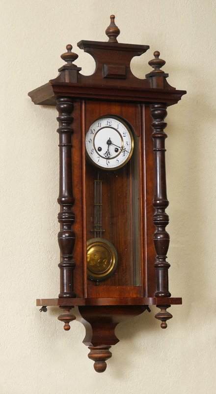 GERMAN WALNUT WALL CLOCK: GERMAN WALNUT WALL CLOCK: Removable pediment, walnut case with applied decoration. Porcelain dial with Arabic numerals. Key wind and pendulum time & strike movement. Overall 36 1/2\" h. x 15 1/4\" x 7