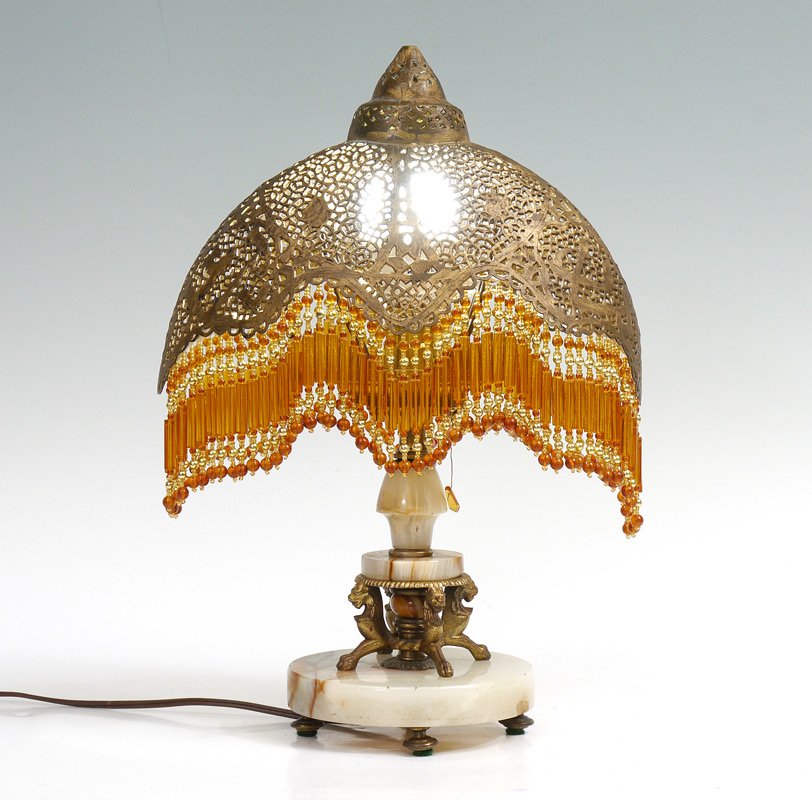 MOROCCAN TABLE LAMP WITH PIERCED SHADE: MOROCCAN TABLE LAMP WITH PIERCED SHADE: Onyx base with figural griffin gilt metal supports. Single socket fixture. Pierced brass shade with beaded fringe marked Made in Syria. Base 10 1/2" h. x 6 1/2"