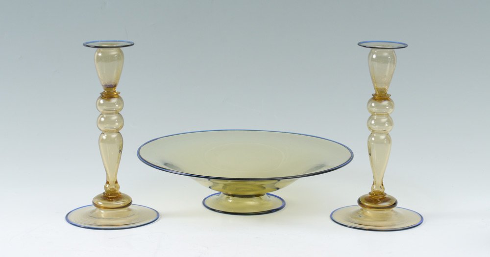 STEUBEN ART GLASS CONSOLE BOWL AND CANDLESTICKS: STEUBEN ART GLASS CONSOLE BOWL AND CANDLESTICKS: Unmarked, amber glass with blue rims to include footed console bowl (3 1/4" h. x 12 1/2"), pair candlesticks (9 3/4" h. x 5 1/4").