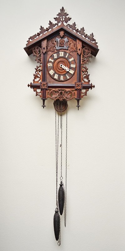 GERMAN CARVED CUCKOO CLOCK: GERMAN CARVED CUCKOO CLOCK: Carved oak leaf crest, walnut case with applied carved decoration. Dial with light wood Roman numerals. Dual pinecone weight driven time and strike movement marked GK with 