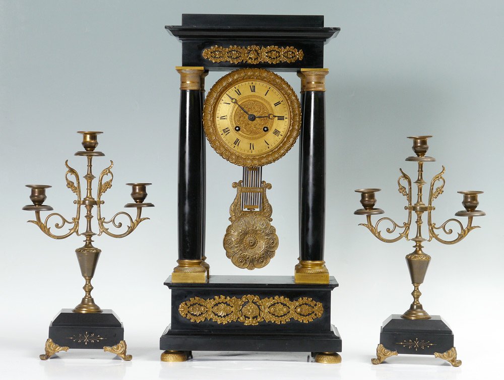 CONTINENTAL BLACK PORTICO CLOCK & GARNITURE: CONTINENTAL BLACK PORTICO CLOCK & GARNITURE: Portico clock with black slate body, applied ormolu decoration, brass dial with Roman numerals. European time and strike movement, embossed pendulum. 21 1/