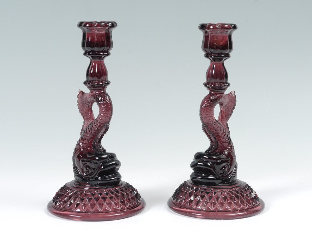 PAIR AMETHYST GLASS DOLPHIN CANDLESTICKS: PAIR AMETHYST GLASS DOLPHIN CANDLESTICKS: Pressed amethyst glass in the form of figural dolphins, each 9 1/2" h. x 5" dia.