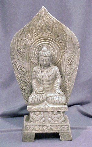 CARVED STONE DEITY STATUE: CARVED STONE DEITY STATUE: This massive solid piece of stone has been carved into a Buddha that is supported on a platform by two figures. A large slab behind Buddha forms into a peak above his head.