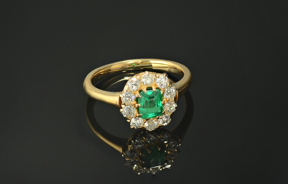 .64 CT EMERALD W/ .60 TW DIAMONDA 18K GOLD RING: EMERALD & DIAMOND VICTORIAN RING: 18K yellow gold ring centering an approx. .64 Ct emerald cut Colombian emerald of VS clarity and 5 saturation. Framed by 10 old European round cut diamonds totaling .