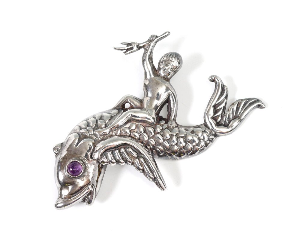 HUBERT HARMON MEXICAN STERLING FIGURAL PIN: HUBERT HARMON MEXICAN STERLING FIGURAL PIN: Figure of a man holding a trident riding a fish with amethyst eye, marked on back with Hubert Harmon, Sterling, Made in Mexico, and baby feet with wings. Me