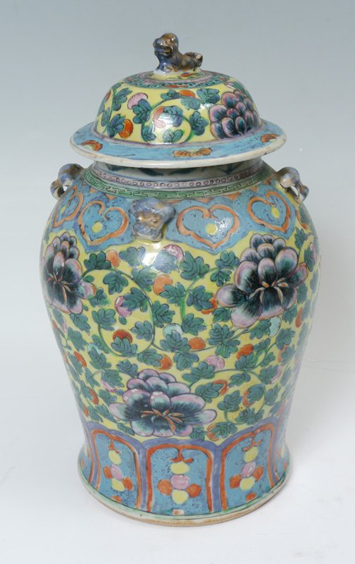 CHINESE POLYCHROME COVERED GINGER JAR: CHINESE POLYCHROME COVERED GINGER JAR: Floral design in a color palette of blues, lavenders, green and orange on a yellow ground. A foo dog finial tops the lid, with four raised foo dog heads spaced a