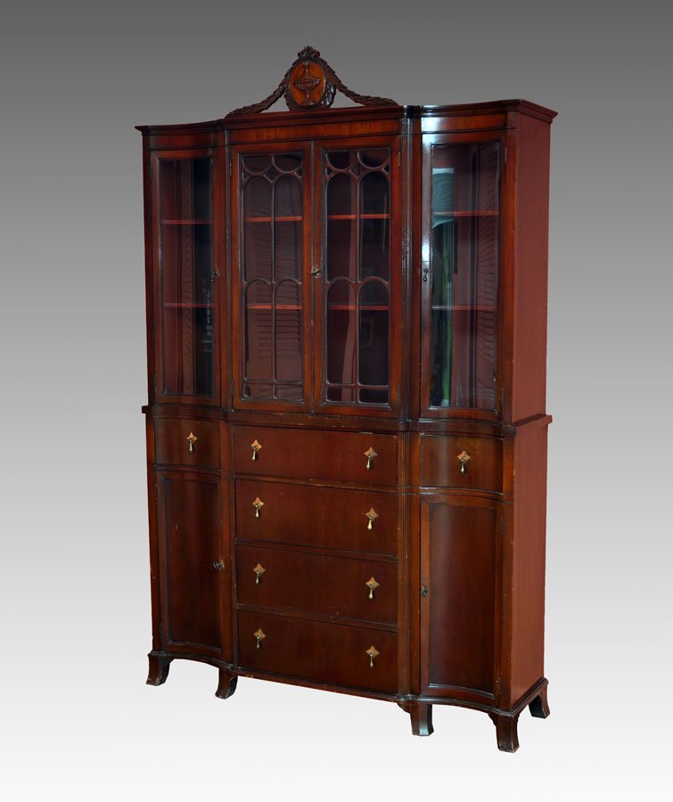MAHOGANY CHINA CABINET: MAHOGANY CHINA CABINET: Carved wreath crest, central medallion with applied urn decoration. 2 central glass doors with fretwork, shaped glass side doors. Base with 4 central drawers, shaped sides with