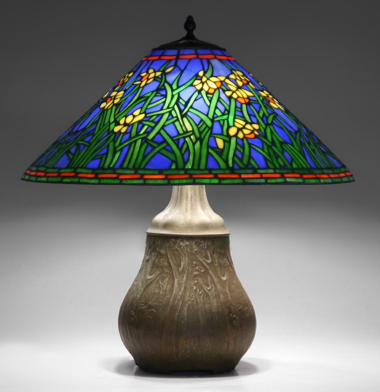 HANDEL LAMP BASE: HANDEL LAMP BASE: Sold with a later leaded glass shade. Signed Handel bulbous patinated metal base with tree trunks in relief, bracket feet. Similar base page 63, "Handel Lamps" by De Falco and Hibel.