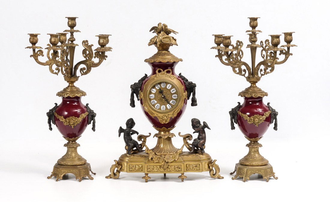 IMPERIAL FIGURAL CHERUB CLOCK GARNITURE SET: IMPERIAL FIGURAL CHERUB CLOCK GARNITURE SET: Contemporary garniture set by Imperial. Clock with red enamel metal case, patinated and gilt metal accents including birds, flowers, lion masquerons and pu