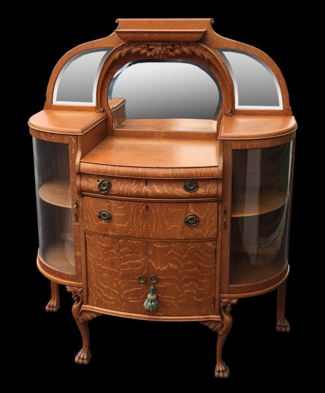 AN UNUSUAL TIGER OAK SIDEBOARD CABINET: Early 20th C., American. Richly grained tiger oak, drop center bowed front of 2 drawers over 2 doors, flanked by bowed glass front display. Gracefully arched backsplash with a trio of beveled mirrors.