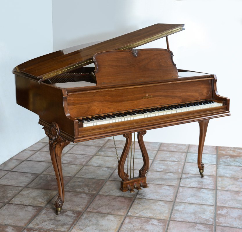 WURLITZER PETITE BABY GRAND PIANO: WURLITZER PETITE BABY GRAND PIANO: Mahogany case, carved and shaped legs with shell and foliate scroll motifs, lyre foot pedal supports. Overall measures 37 1/4'' h. x 57 1/2'' x 54''. Sold with match