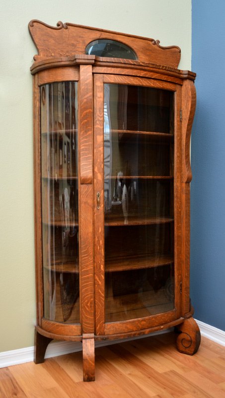 TIGER OAK TRIPLE BOWFRONT CABINET: TIGER OAK TRIPLE BOWFRONT CABINET: Carved and shaped top backsplash with oval beveled glass mirror, 4 wood shelf interior, scroll front feet. Overall measures 73 1/2'' h. x 39'' x 17''.