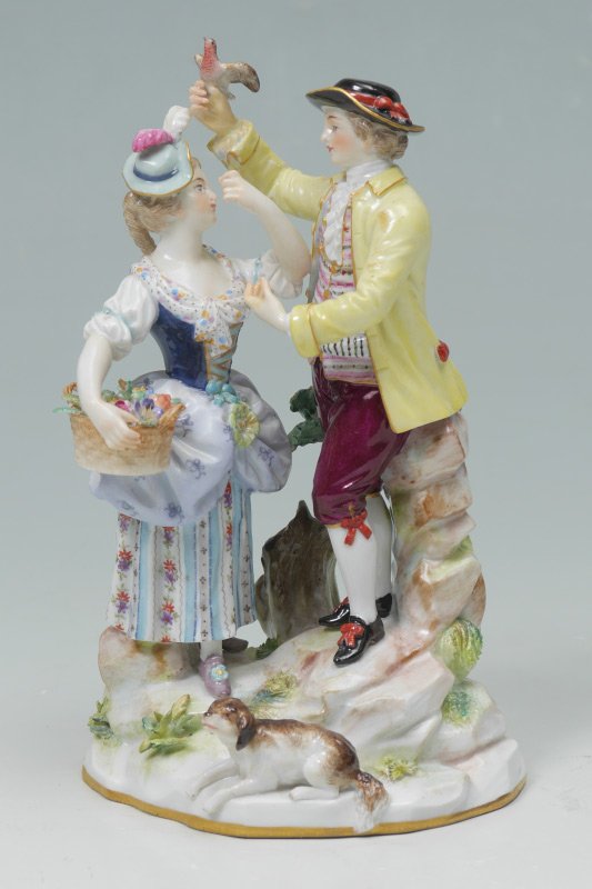 MEISSEN PORCELAIN COUPLE FIGURE: MEISSEN PORCELAIN COUPLE FIGURE: Figural group of a man holding a bird and a woman holding a basket of flowers and a dog. Blue crossed swords Meissen mark on base, 6 1/2" h. x 4".