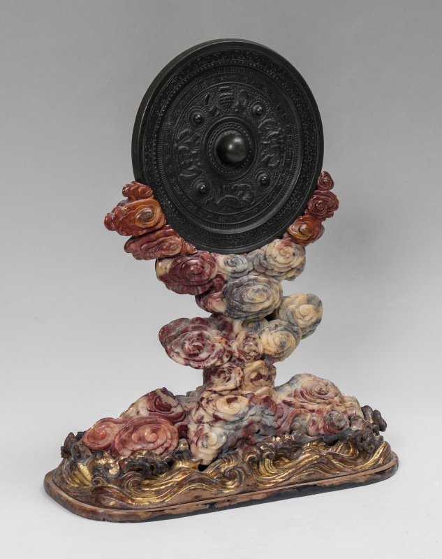 CHINESE HAN DYNASTY BRONZE MIRROR WITH STAND: CHINESE HAN DYNASTY BRONZE MIRROR WITH STAND: Silvered bronze mirror with figures of seated royalty, dragon and fruit tree, encircled with writing, 7 3/4''. Sold with a carved soapstone stand with flo